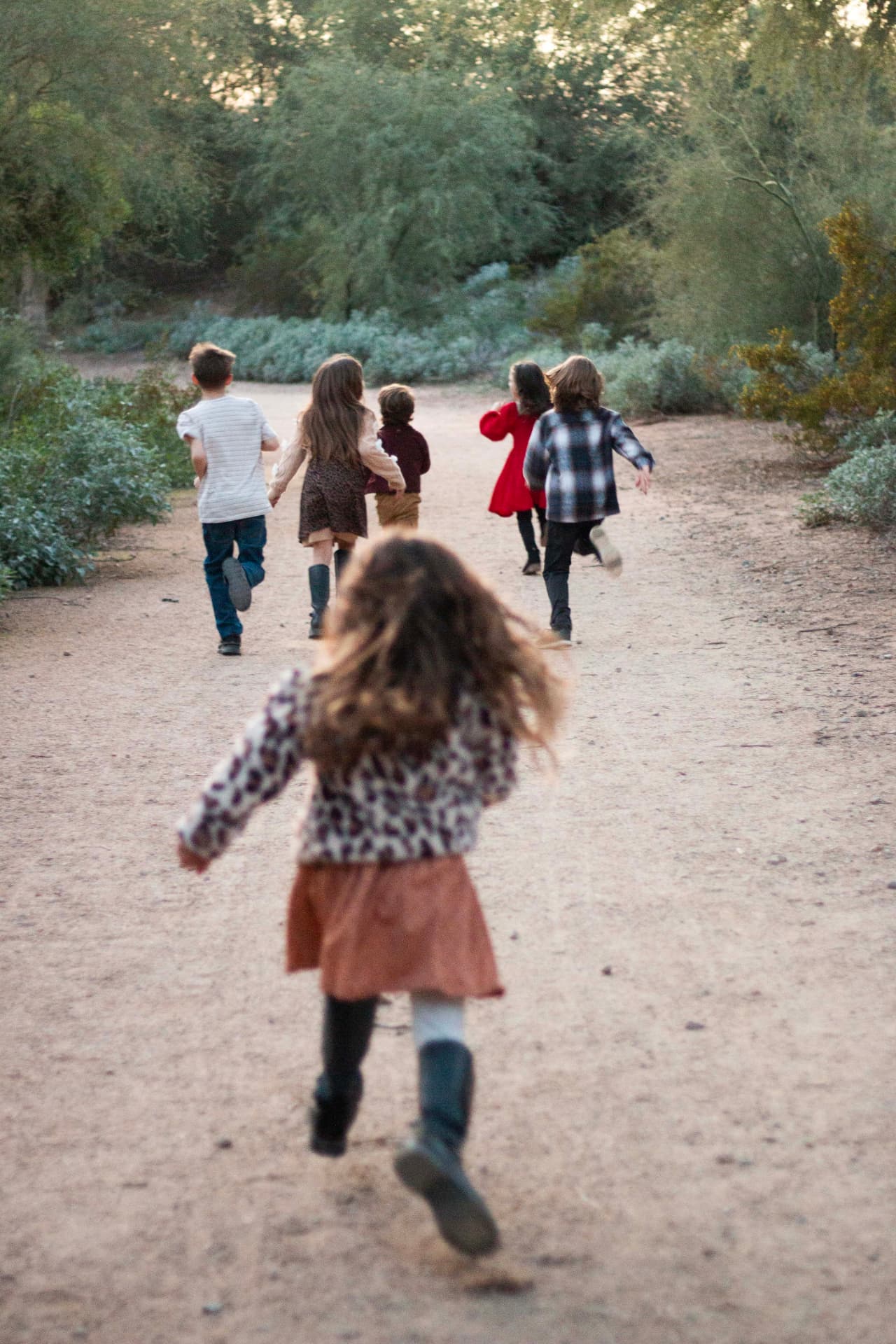 Six children running joyfully down a dirt path away from the camera