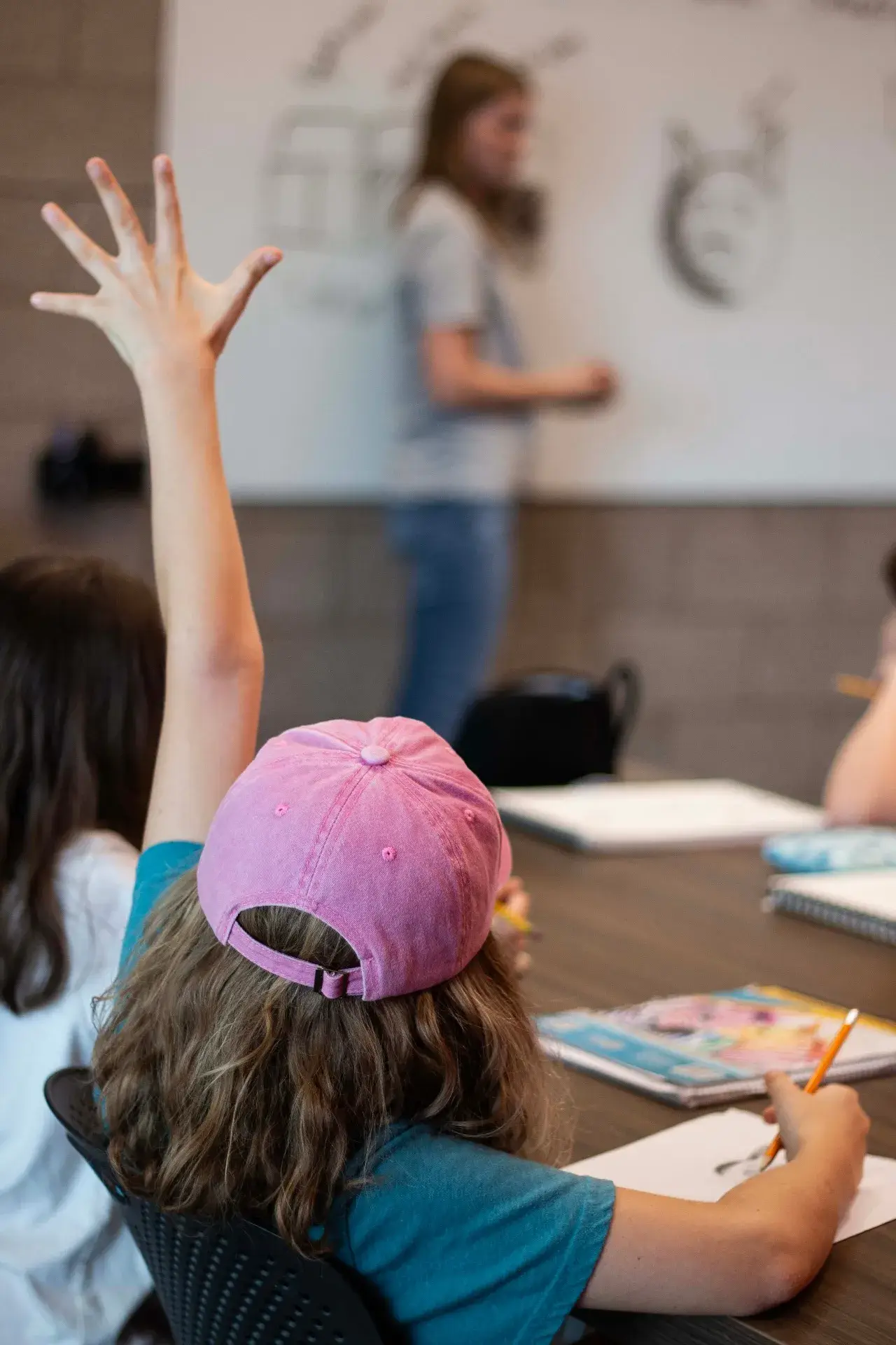 Child in a pink cap raising a hand during class